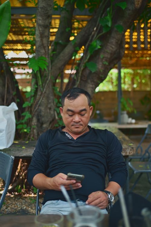 Free A man sits outdoors using his smartphone, surrounded by greenery, in a relaxed setting. Stock Photo