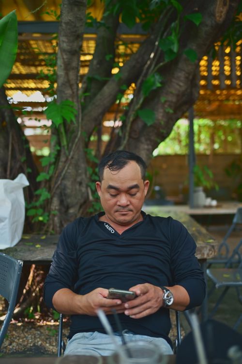 Free Adult man in a casual outdoor setting, engaged with a smartphone, under a tree. Stock Photo
