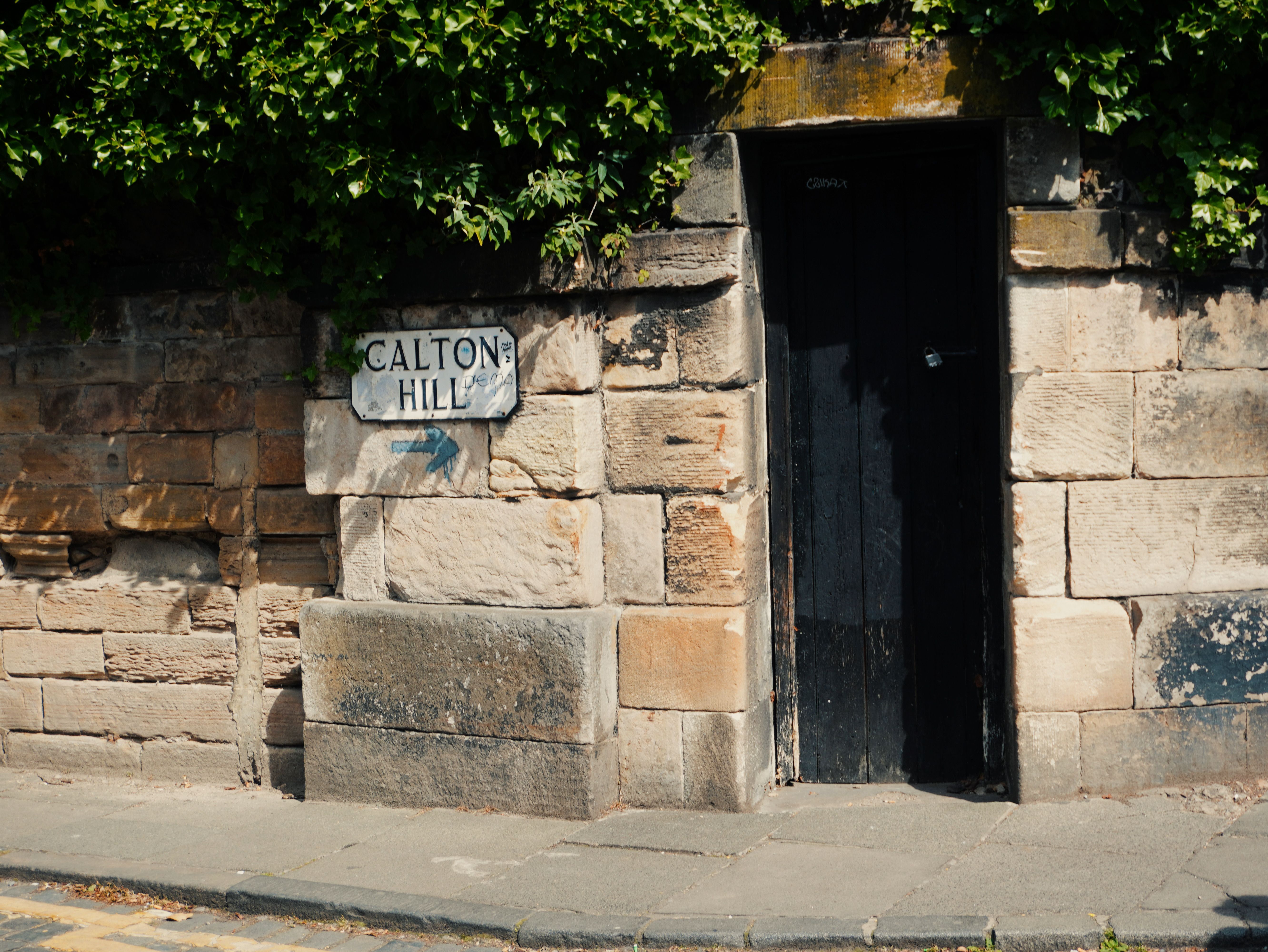 Stone wall with Calton Hill sign and black door in Edinburgh, Scotland, UK