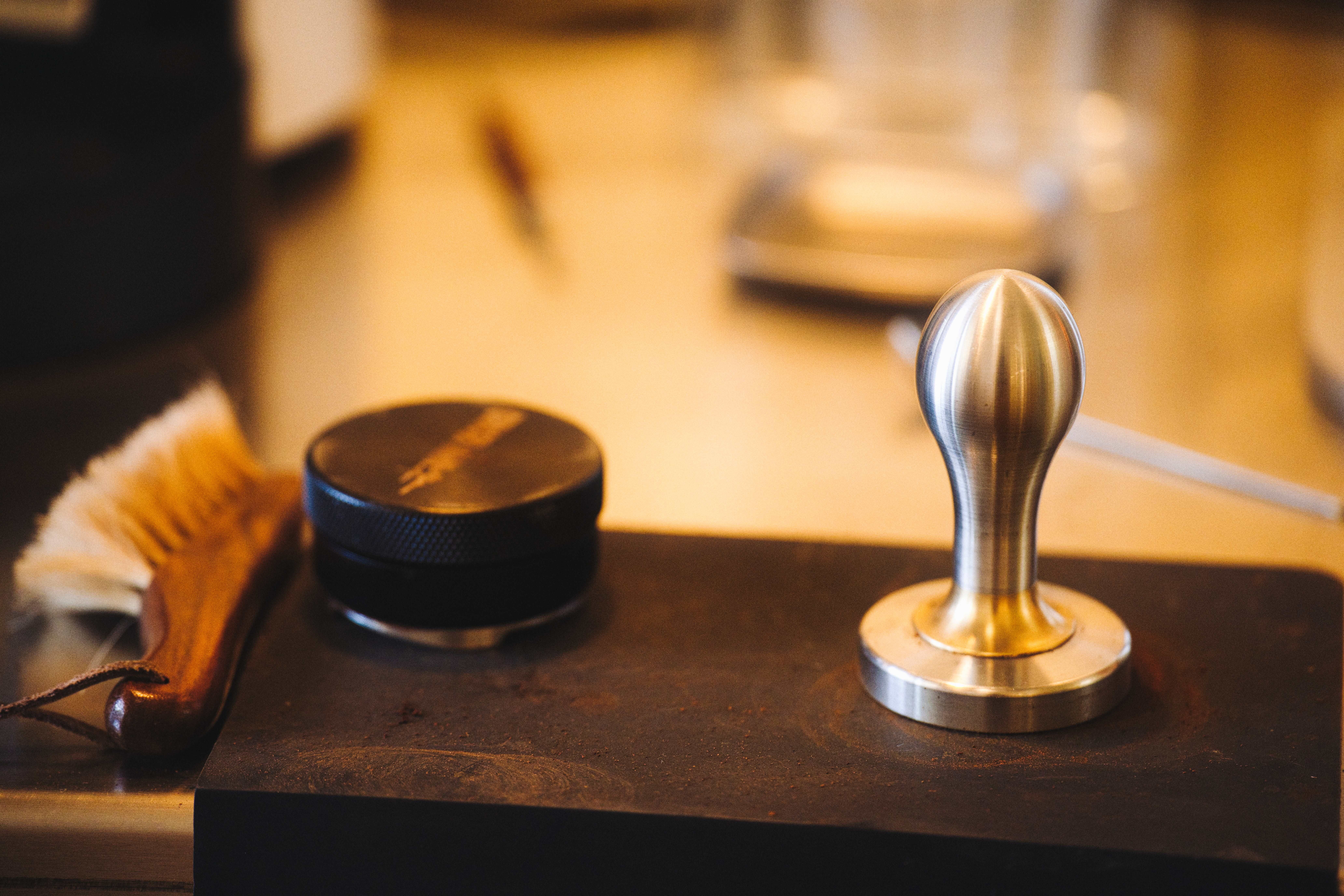 A detailed close-up image of a coffee tamp with brush and tools on a barista counter, ideal for cafe themes.