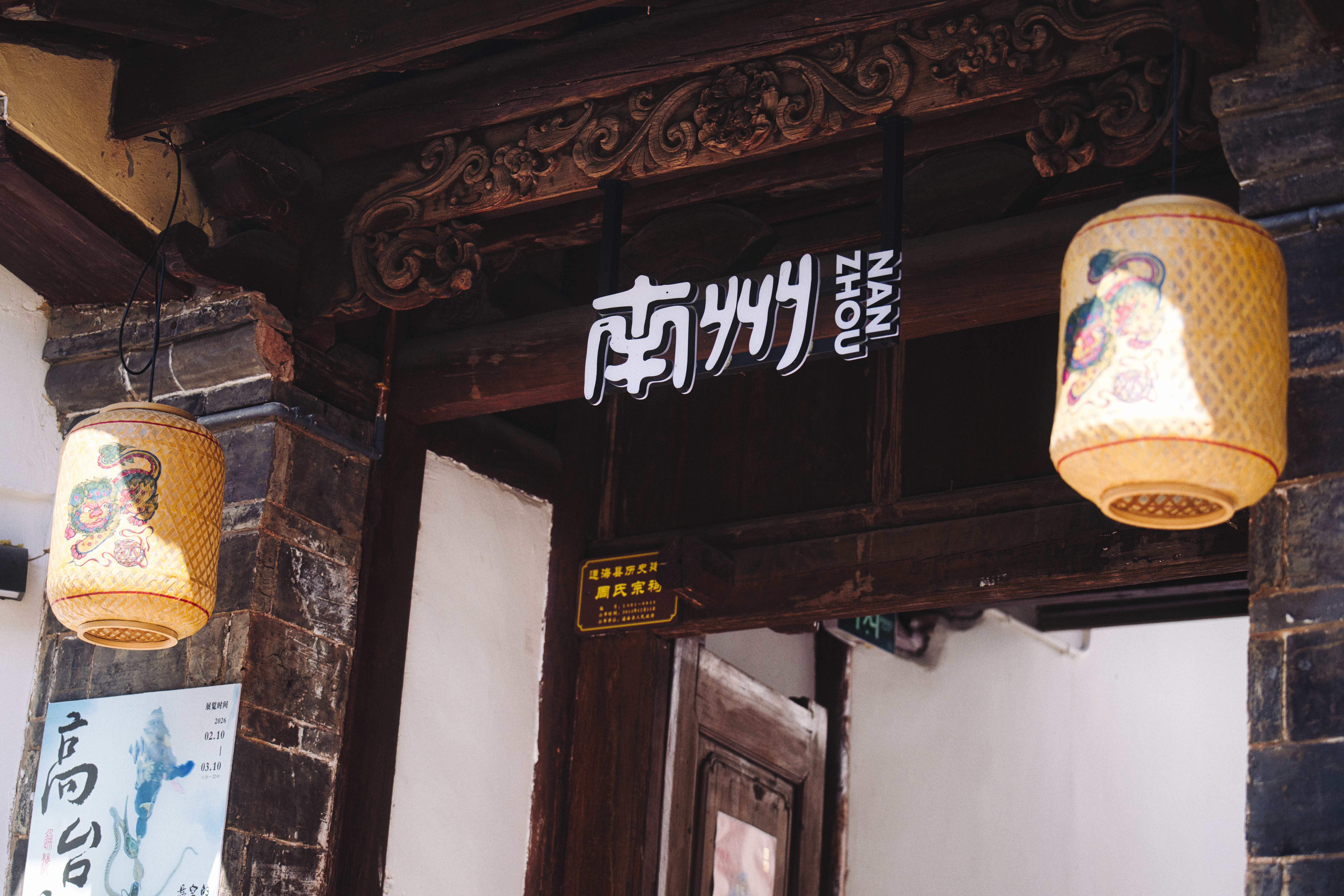 A close-up of traditional Chinese lanterns hanging from an ornately carved wooden doorframe with signs.
