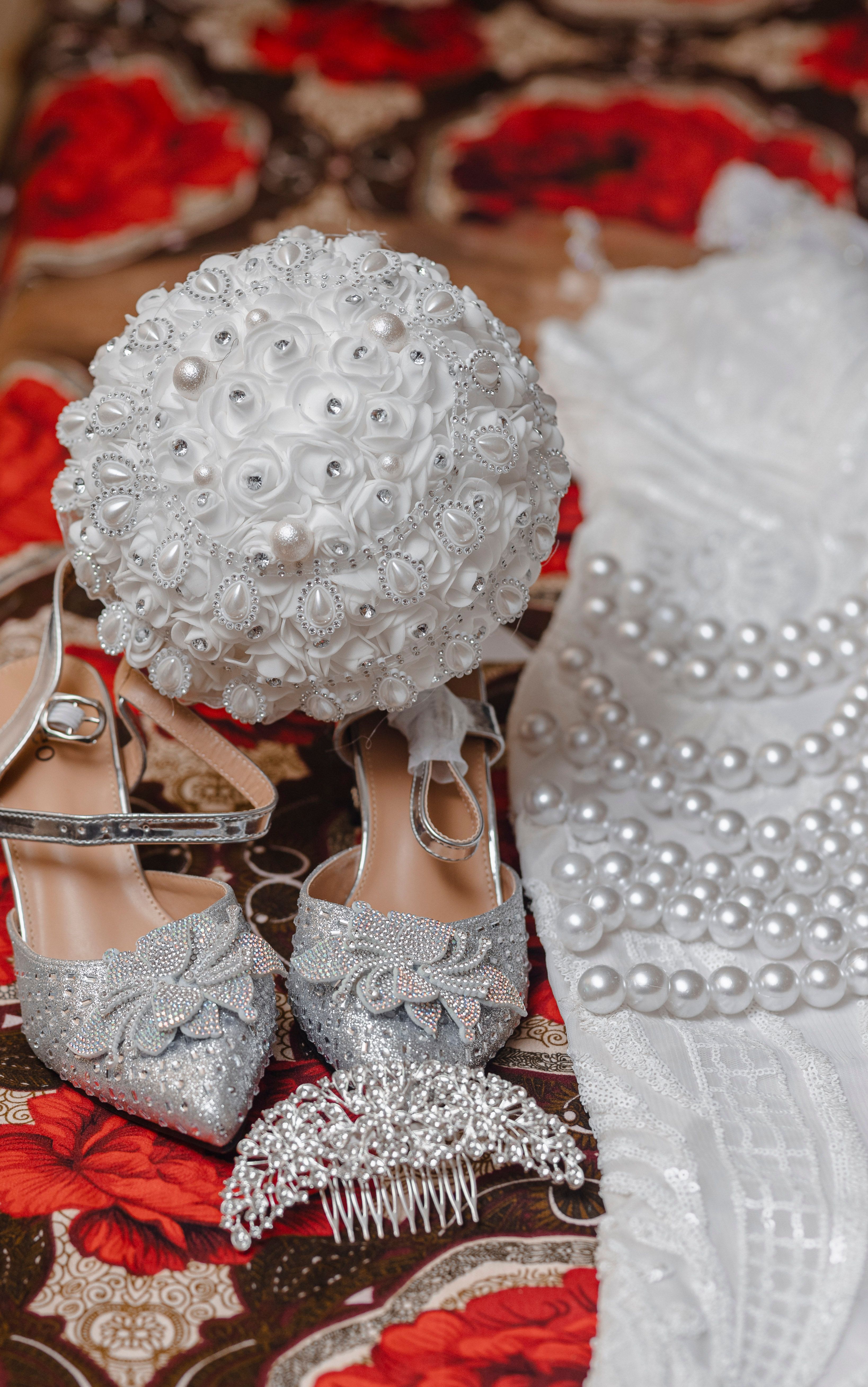 Bridal accessories including silver shoes, lace bouquet, and pearls on a floral background.