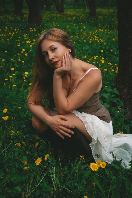 Free A young woman in a dress sitting gracefully in a meadow filled with yellow flowers. Stock Photo