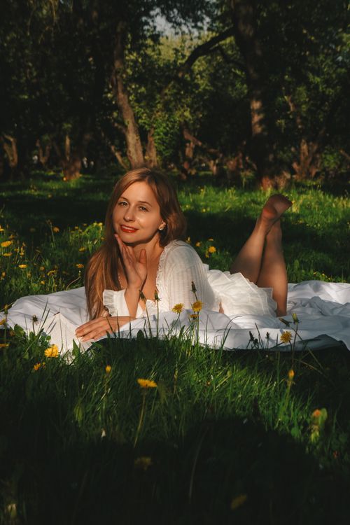 Free A relaxed young woman in a white dress enjoying a sunny day in a lush green meadow with dandelions. Stock Photo