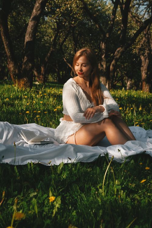 Free Young woman enjoying a peaceful picnic in a sunlit meadow surrounded by blooming dandelions. Stock Photo