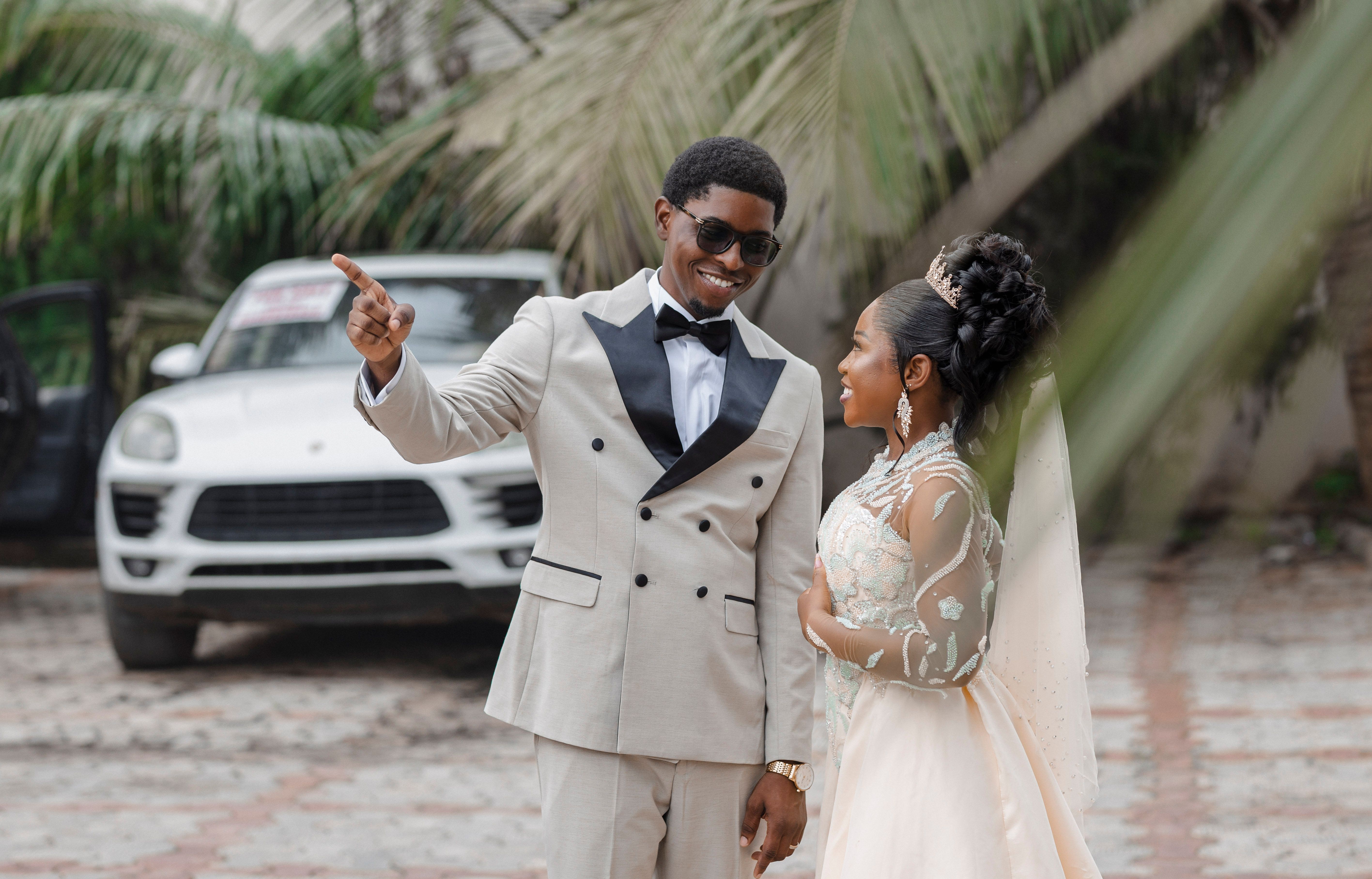 Stylish couple enjoying their wedding day outdoors with a parked car backdrop.