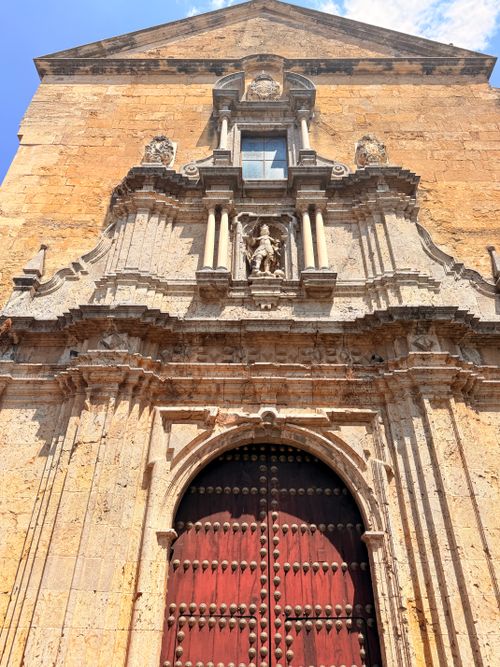 Free Baroque-style facade of an old building in Spain with detailed sculptures and red wooden door. Stock Photo