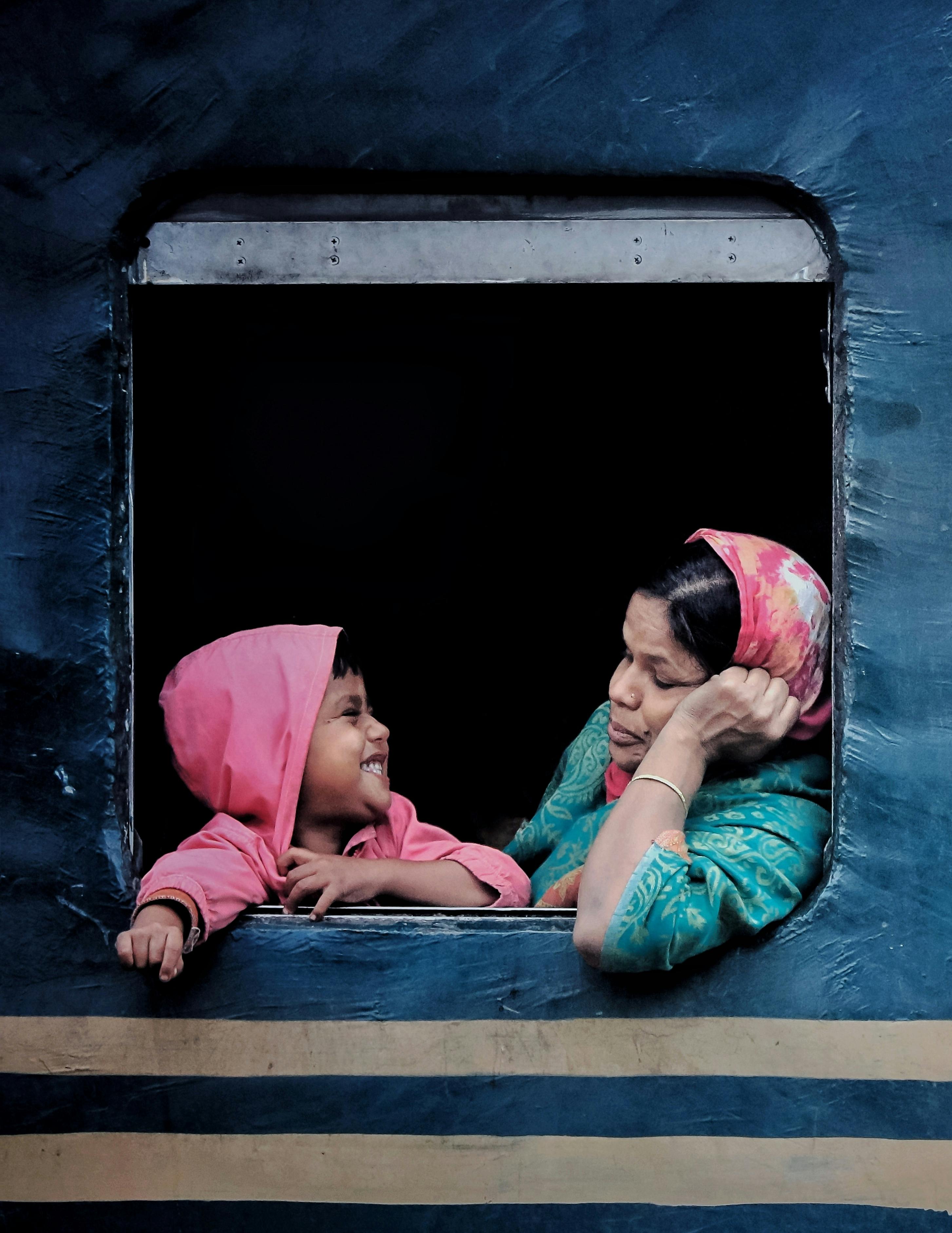 A touching moment of a mother and child sharing smiles through a train window, capturing warmth and connection.