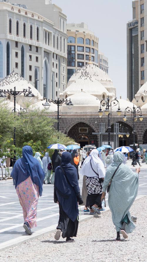 Free View of people walking near a historic mosque in Madinah, showcasing Islamic architecture and daily life. Stock Photo