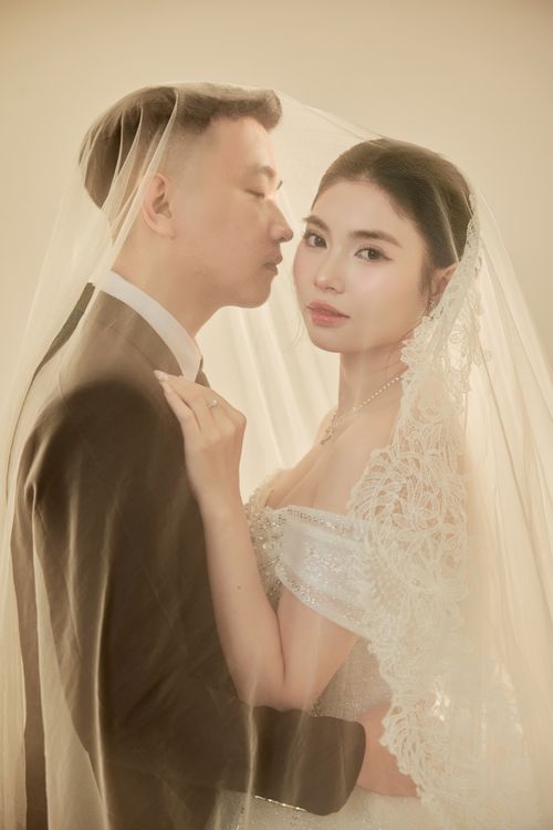 Free Bride and groom tenderly posed under a delicate veil capturing timeless romance. Stock Photo