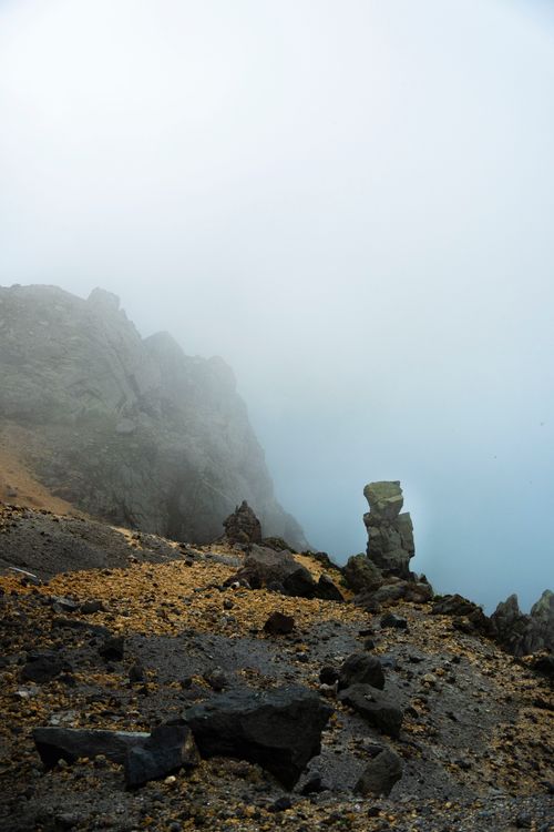 Free A dramatic rocky cliff enveloped in thick mist, creating a mysterious and serene atmosphere. Stock Photo