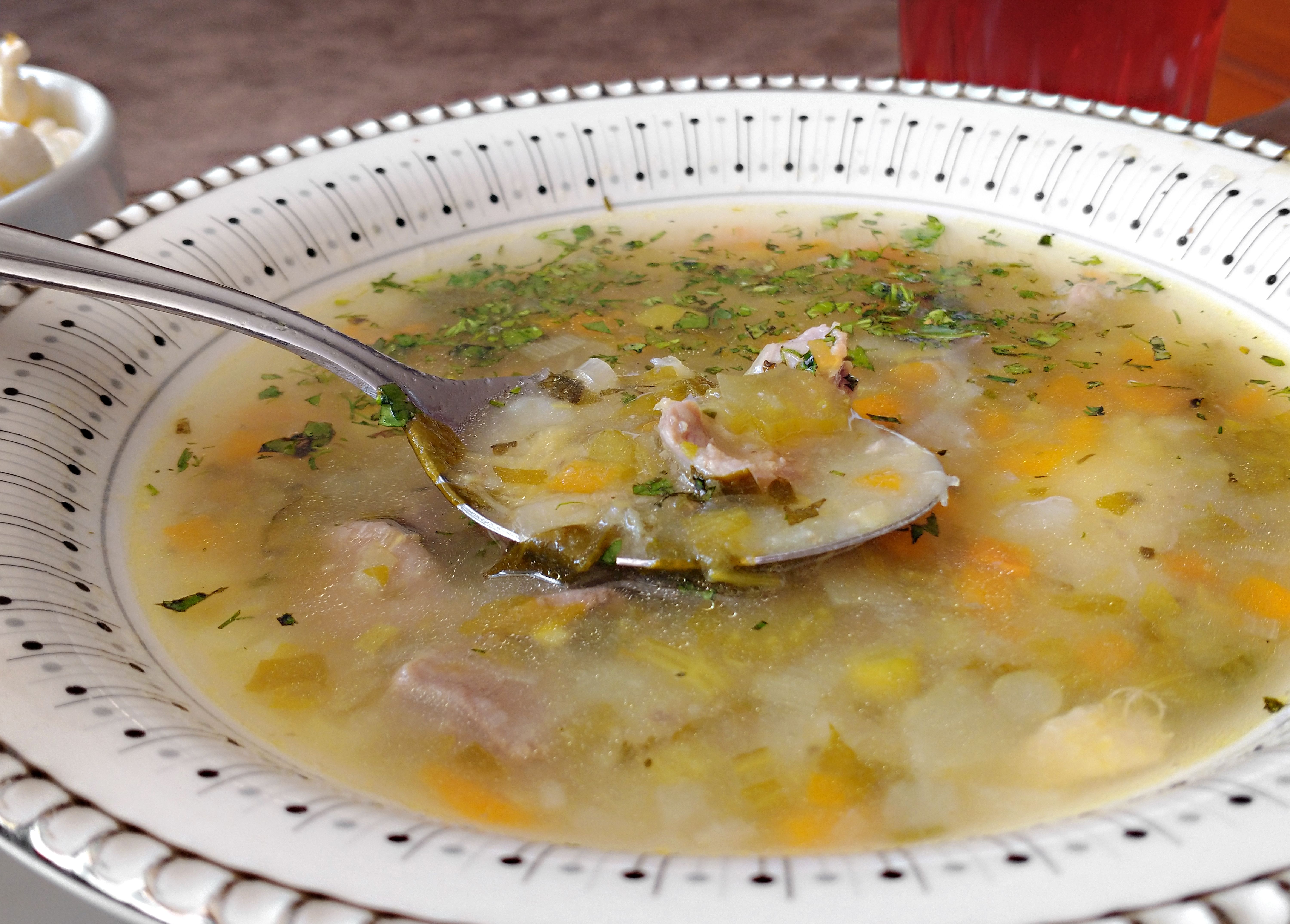 A hot bowl of rustic game soup served in a dark clay bowl.
