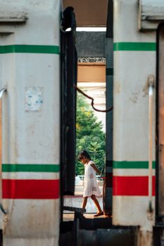 A young girl walks between parked train carriages at a railway station, framed by the gap.