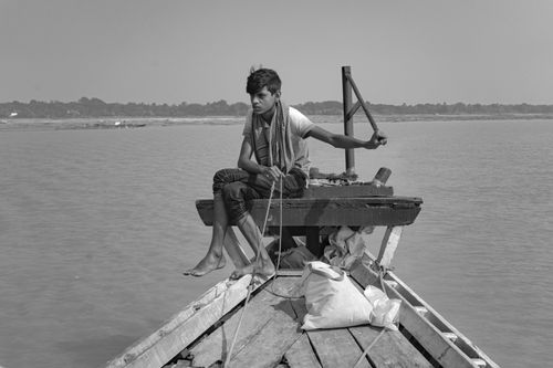 Free A young man sits thoughtfully on a wooden boat in a calm river scene. Stock Photo