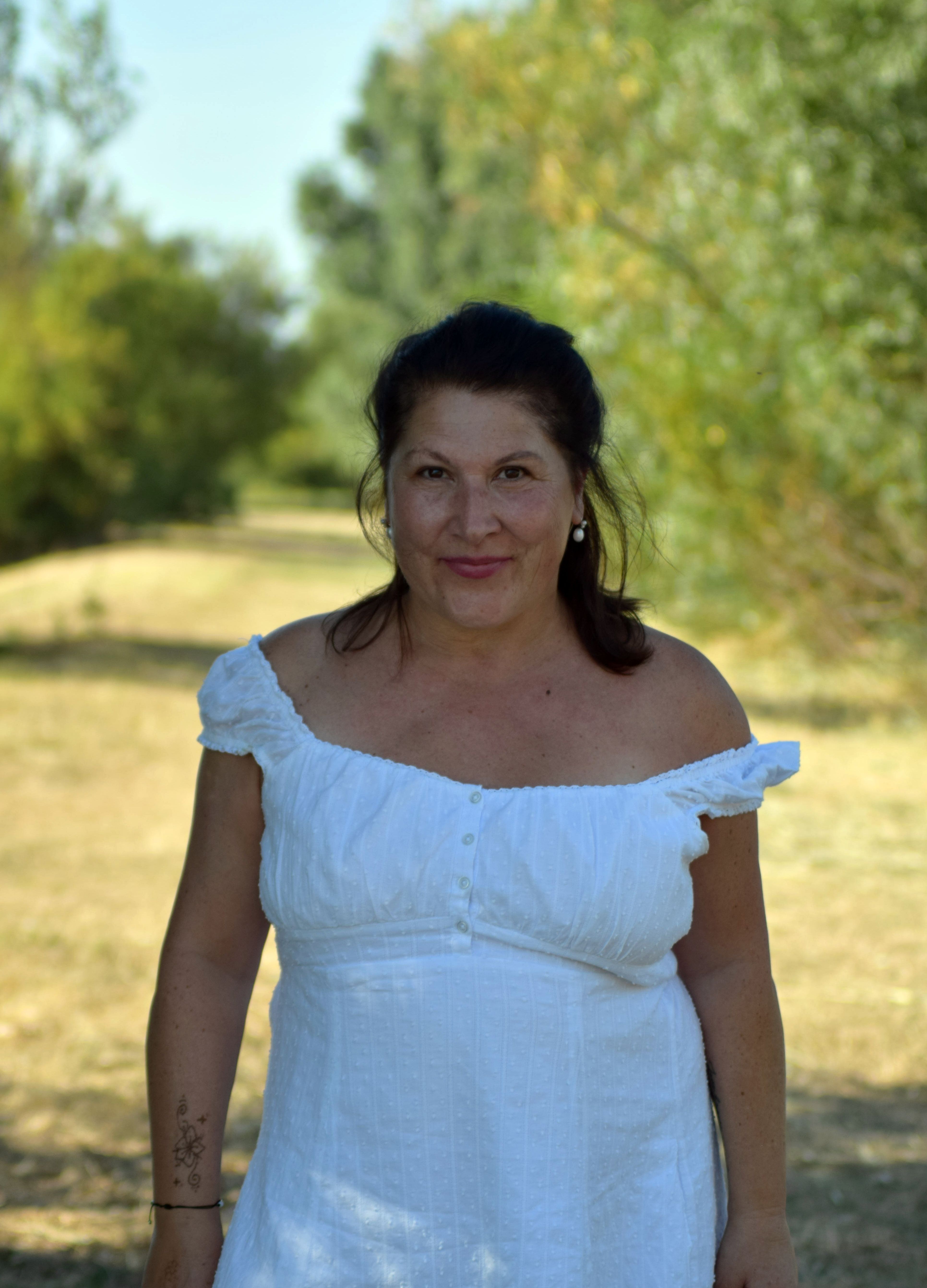 A cheerful woman in a white dress enjoying a sunny day outdoors.