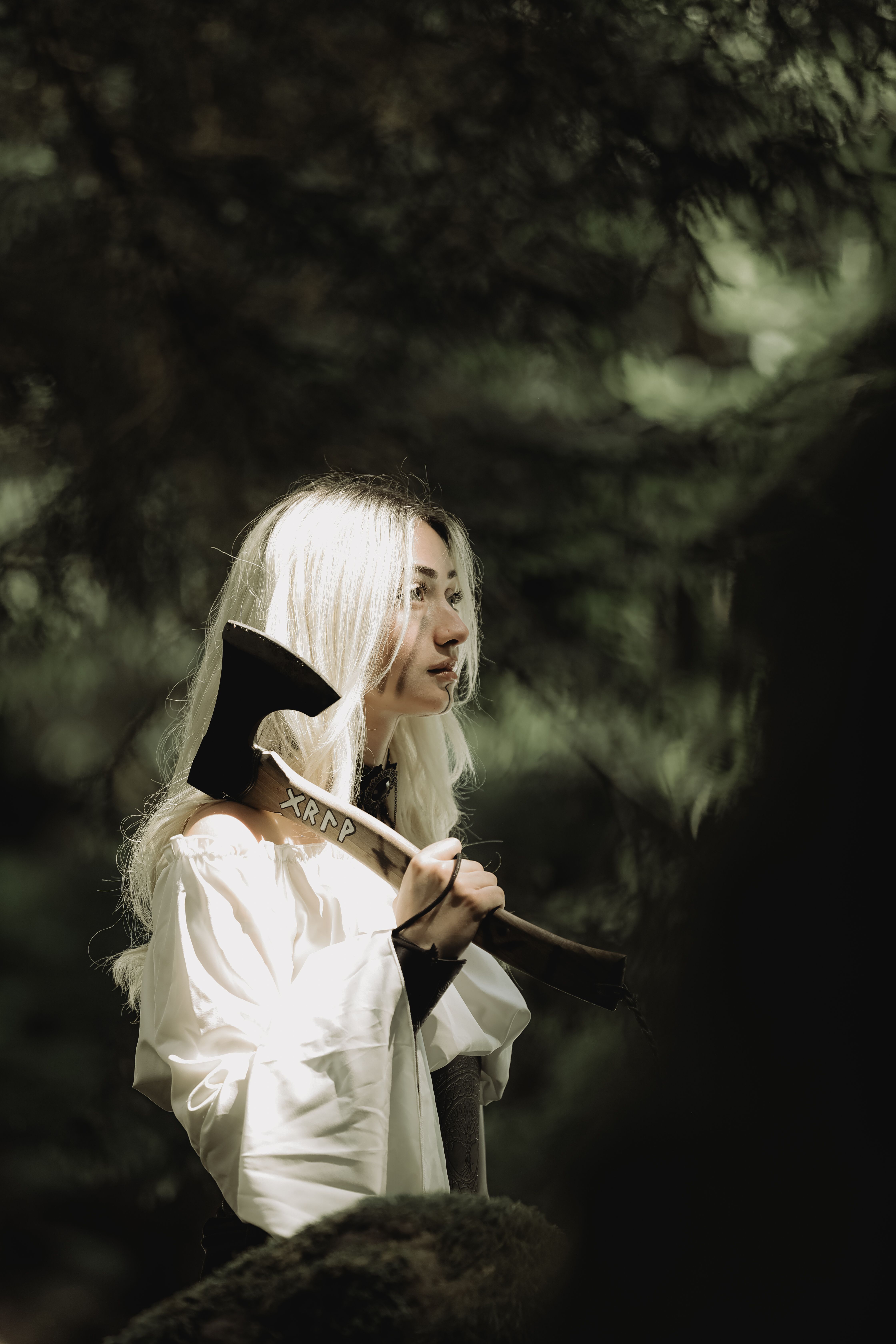 A young woman holding an axe in a peaceful, forested environment.