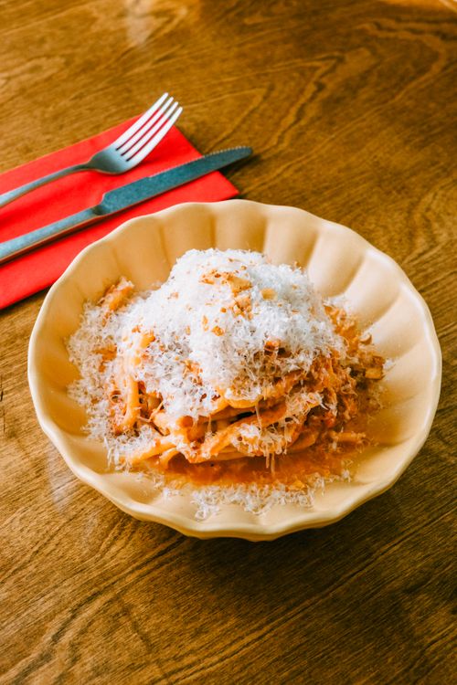 Free Delicious spaghetti with rich tomato sauce topped with grated Parmesan cheese on a wooden table. Stock Photo