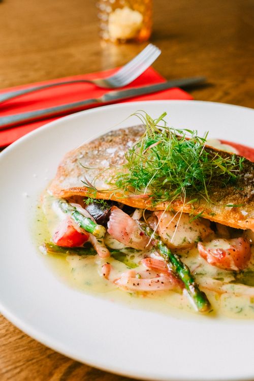 Free Plate of grilled fish with asparagus, tomato, and greens in a cozy restaurant setting. Stock Photo