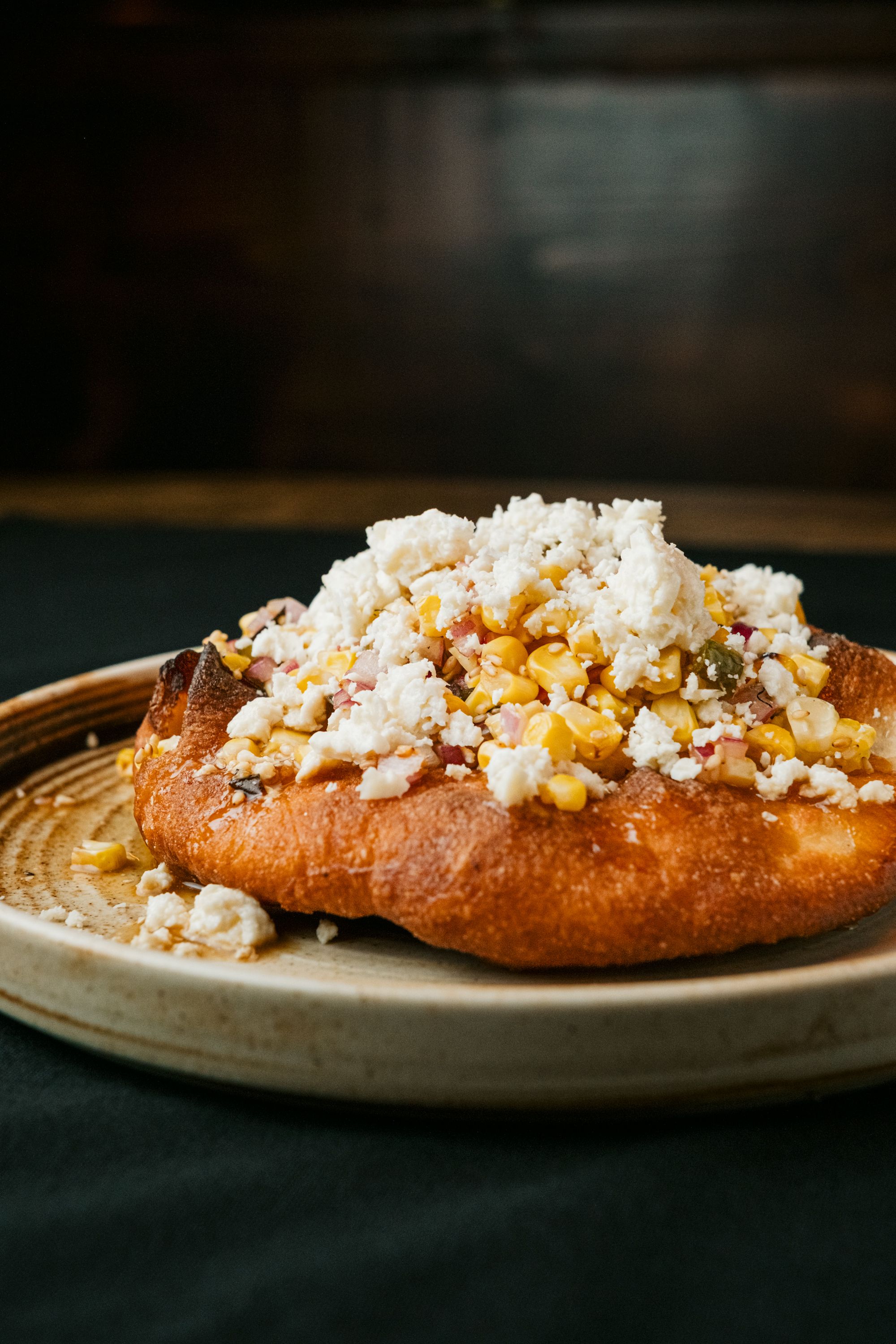 A stack of golden brown fry bread rounds with a crisp, bubbled crust, one piece torn open to show the soft chewy interior, next to a small bowl of honey.