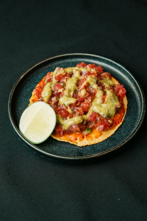 Free A vibrant tuna tostada topped with fresh avocado sauce and a lime wedge on a dark plate. Stock Photo