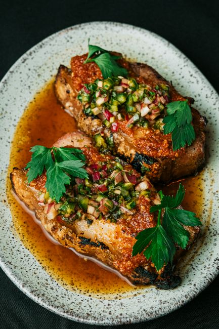 A raw pork shoulder generously coated in a reddish-brown spice rub resting on a wire rack, with a small bowl of the mixed brown sugar and paprika rub set beside it.