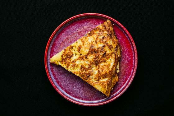 Thick wedge of golden Spanish potato tortilla with browned top on a red plate