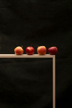 A minimalist still life of apples on a wooden table against a dark background.