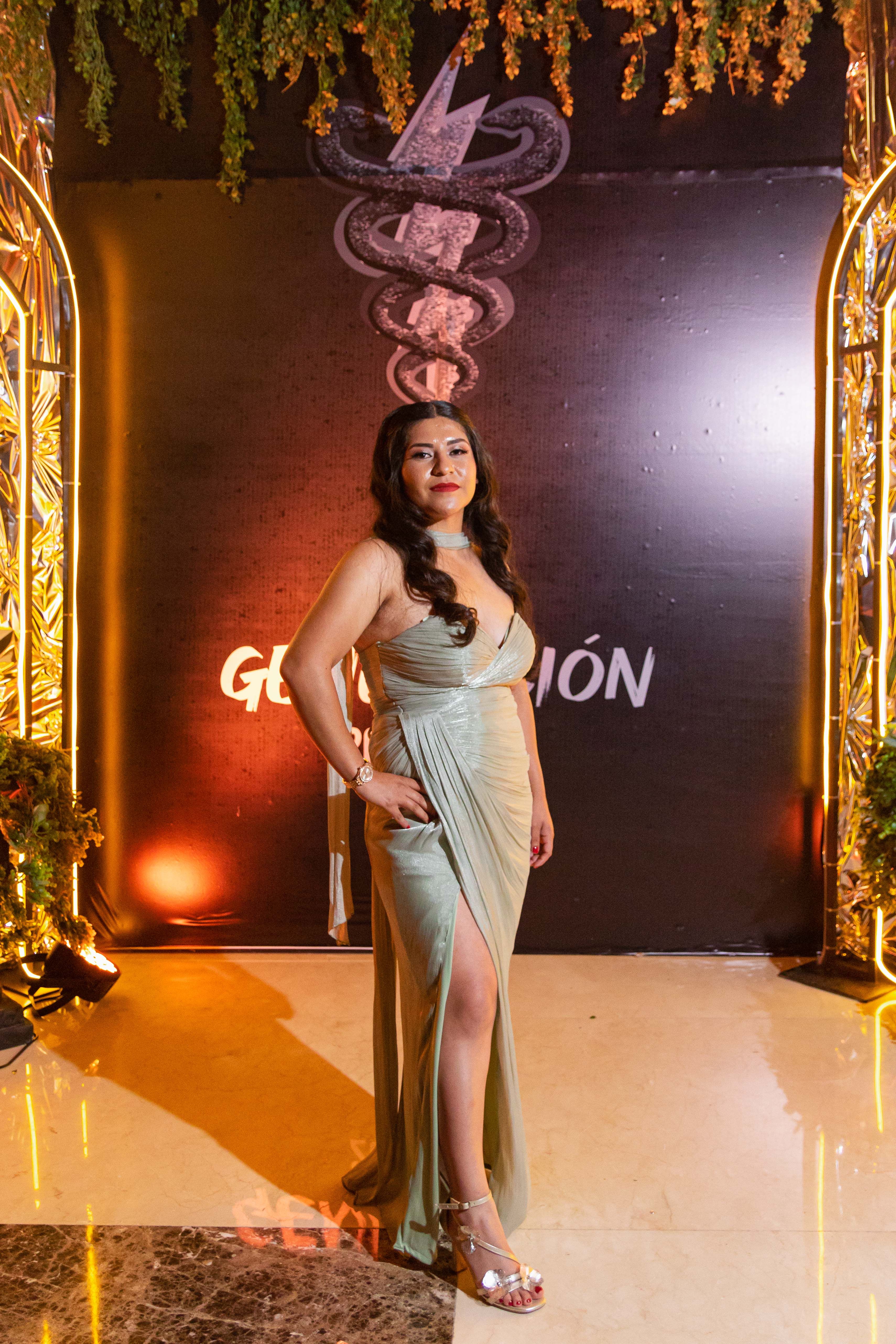 Stylish woman in an elegant gown poses at a formal indoor event with dramatic lighting.
