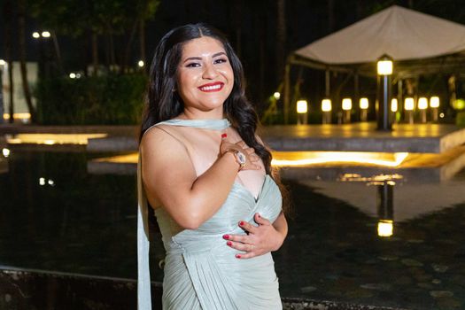 Elegant woman in evening gown smiles near illuminated pool at night. Perfect for lifestyle and fashion themes.