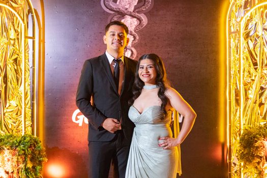 A smiling couple in formal evening wear at a glamorous party with warm lighting.