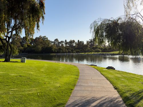 Free A tranquil park pathway curves along a serene lake, surrounded by lush greenery in Irvine, California. Stock Photo