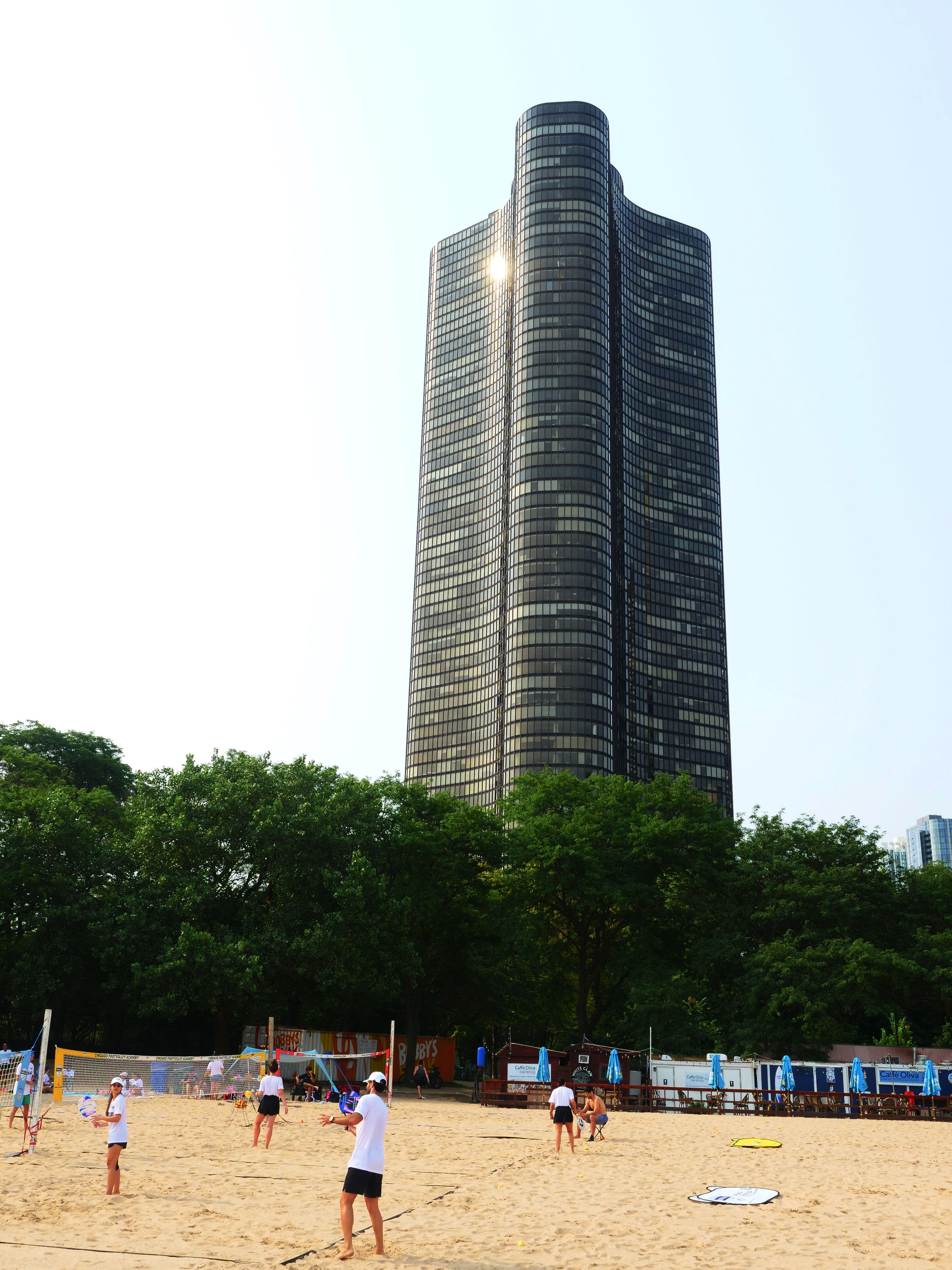 Partido de voleibol de playa cerca del icónico Lake Point Tower en Chicago con jugadores disfrutando de un día soleado.