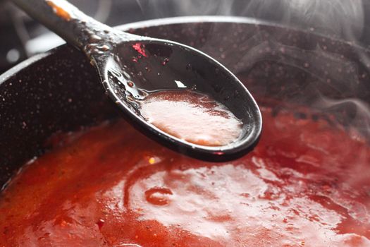 Steamy tomato sauce cooking in a pan with a ladle scooping a portion.