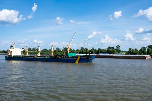 Free A cargo ship navigates the Mekong River surrounded by a lush green forest under a clear blue sky. Stock Photo