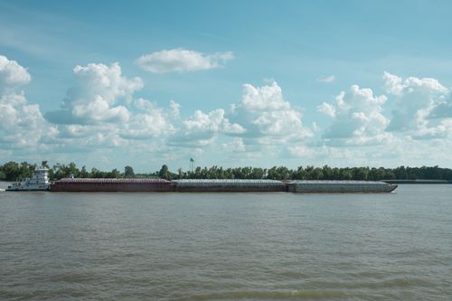 Free Wide view of a cargo barge navigating a large river on a clear day with fluffy clouds overhead. Stock Photo