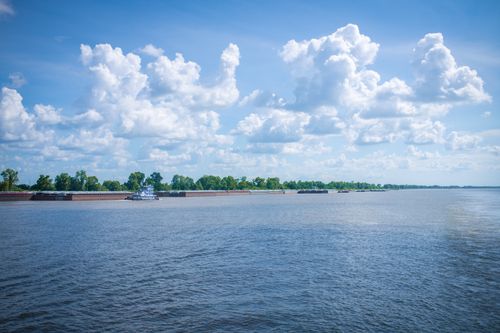 Free Scenic view of a large river with a boat and fluffy clouds in a blue sky. Stock Photo