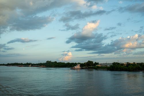 Free A tranquil river view with tugboats and lush greenery under a colorful sky at sunset. Stock Photo