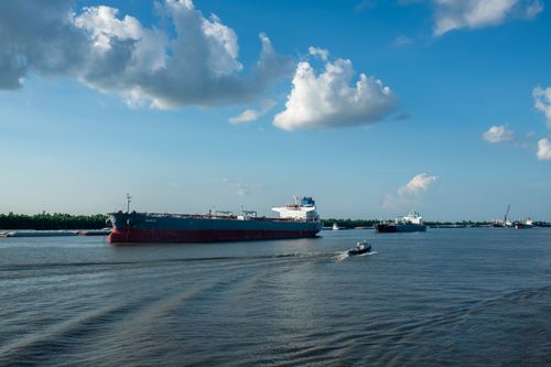 Free Cargo ships and a tugboat navigating a wide river under a clear blue sky with scattered clouds. Stock Photo