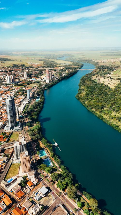Free Stunning aerial view of a river flowing through a vibrant city with lush greenery and clear skies. Stock Photo