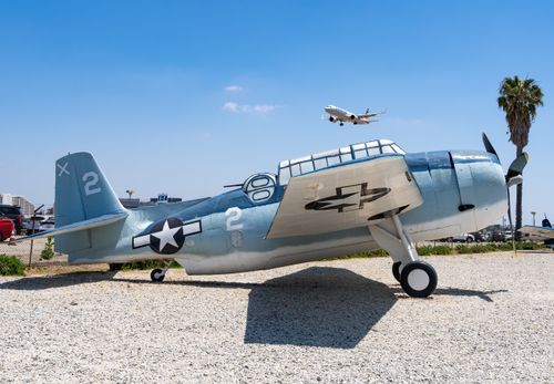 Free Vintage WWII aircraft on display outdoors with a plane flying overhead on a sunny day. Stock Photo