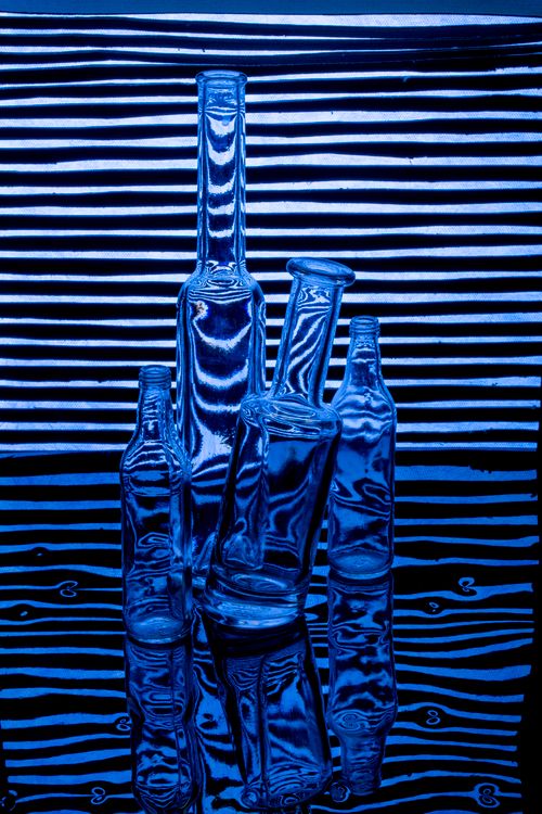 Free Artistic photograph of abstract blue glass bottles on a reflective striped surface. Stock Photo