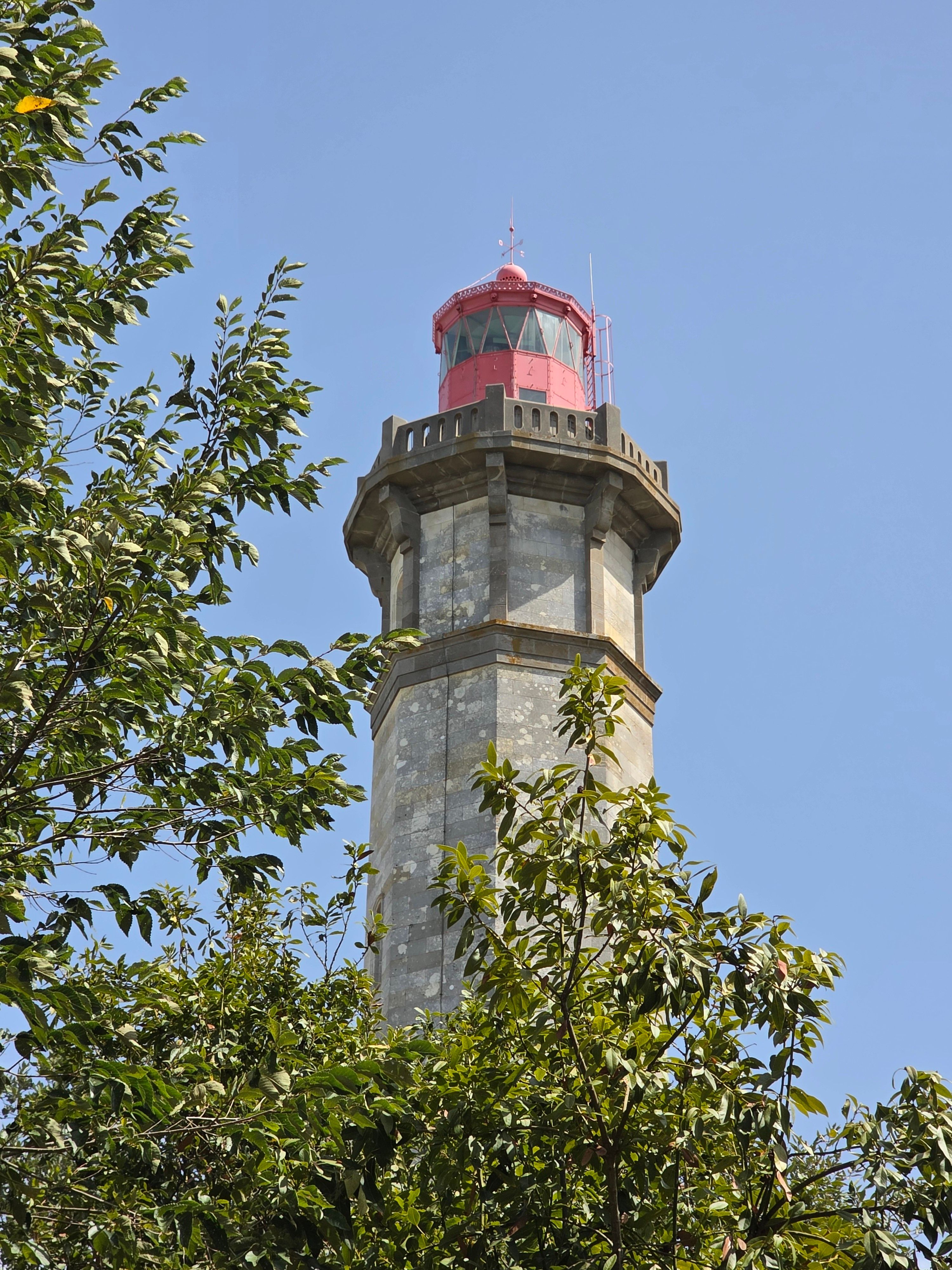 A scenic view of a historic lighthouse surrounded by lush greenery under a clear blue sky.