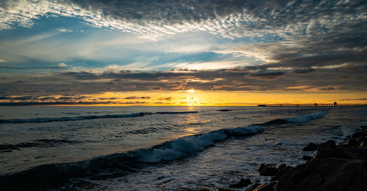 Stunning sunset over Oceanside Pier in California, capturing waves and clouds.