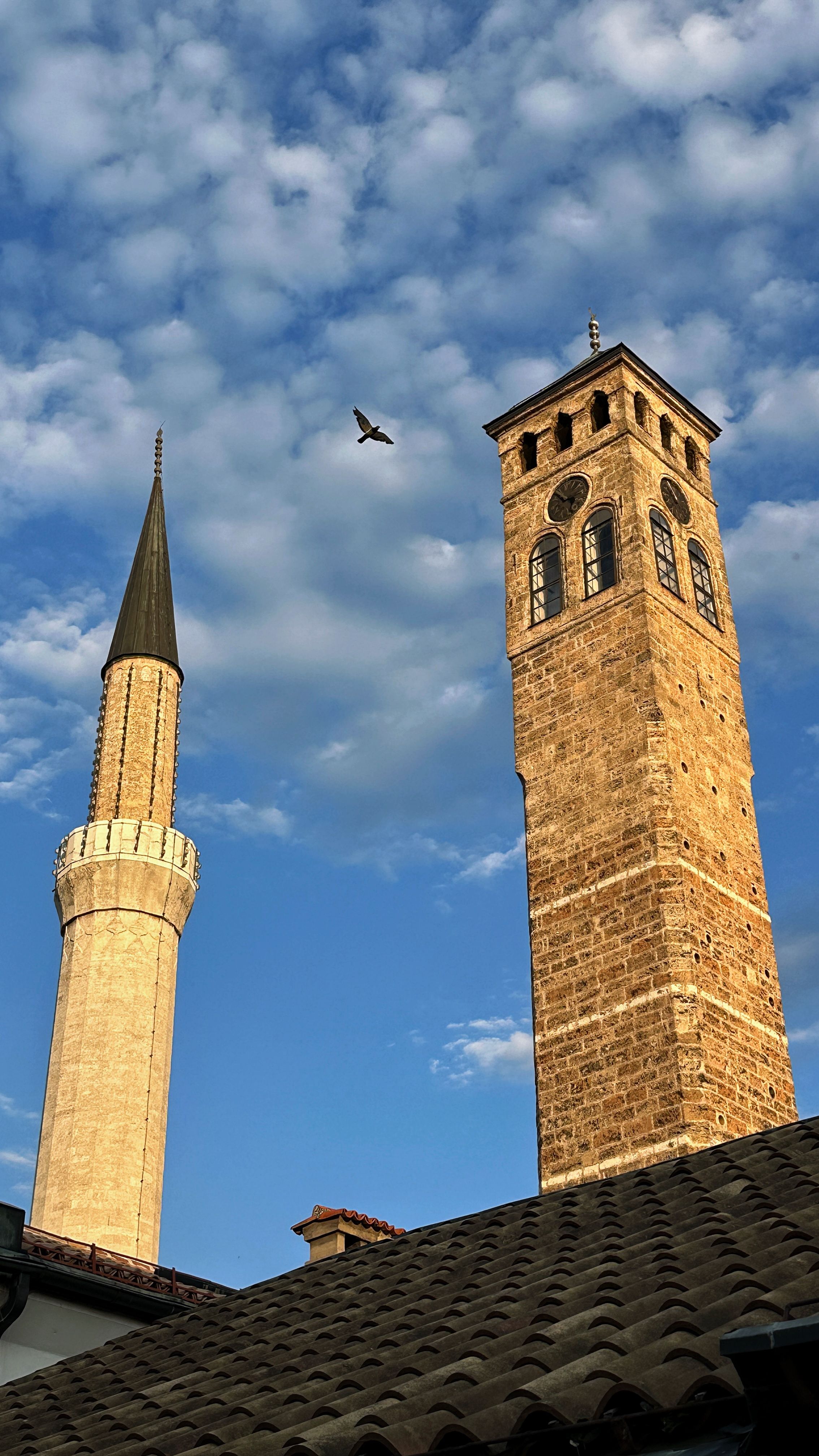 View of Gazi Husrev-beg Mosque minaret and the iconic clock tower in Sarajevo under a clear blue sky.