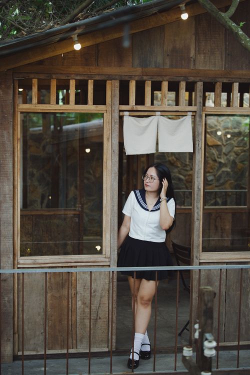 Free Young woman in school uniform posing at a rustic wooden cabin, creating a serene and nostalgic atmosphere. Stock Photo