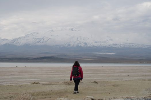A lone hiker stands by a vast lake with snowcapped mountains in the background, embracing nature's magnificence.