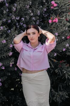 A young woman in pink attire posing against a vibrant flowering bush outdoors.