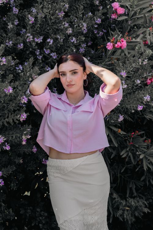 Free A young woman in pink attire posing against a vibrant flowering bush outdoors. Stock Photo