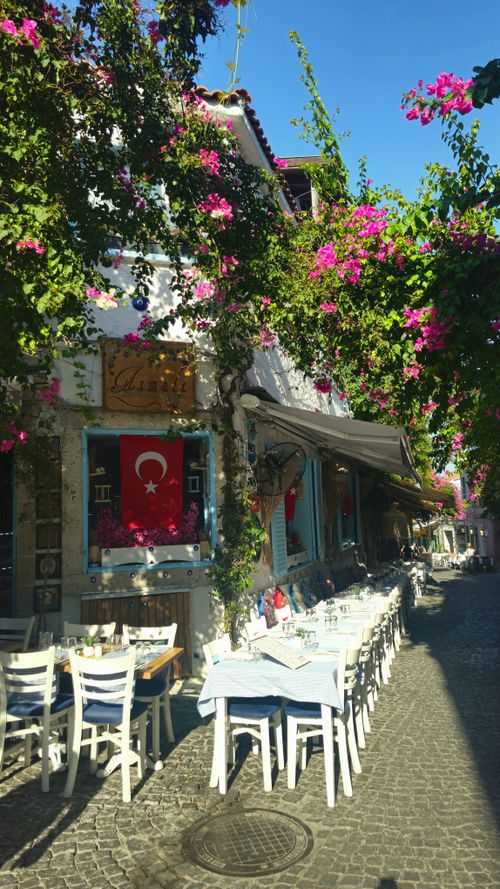 Free Quaint outdoor cafe on a sunny day in Alaçatı, Türkiye, adorned with vibrant flowers and Turkish flag. Stock Photo