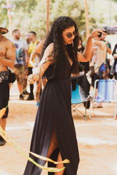 A woman in a black dress dances joyfully at an outdoor festival on a sunny day.
